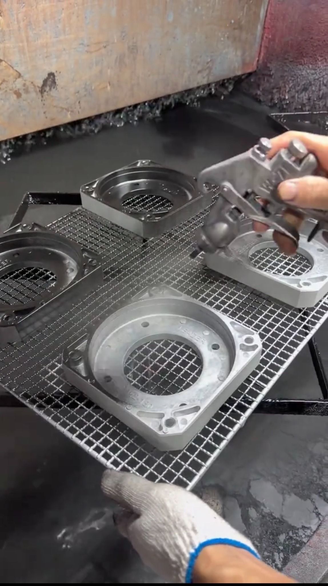 Spray painting aluminum die cast parts with a spray gun, showing liquid coating being atomized and deposited on the part surface.