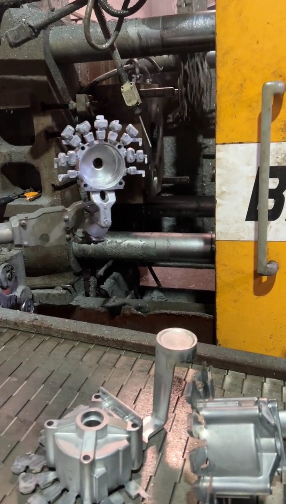 Die casting machine opened during production with aluminum housing type parts visible in front of the machine
